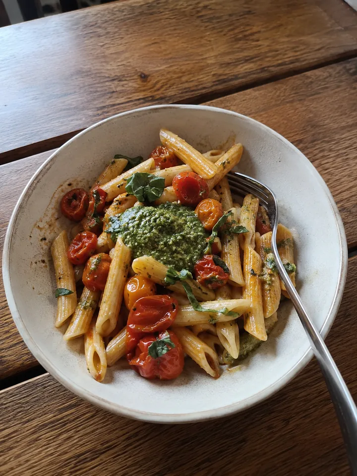 A bowl of penne with tomatoes and pesto on a wooden table